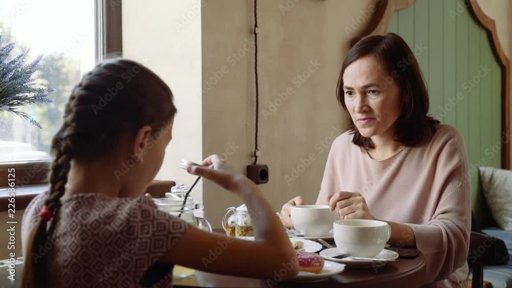 Happy woman in a cafe drinking tea with her 10 year old daughter.