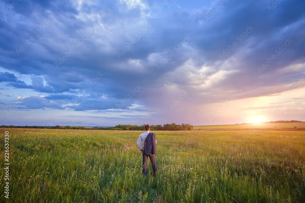 Businessman in elegant suit with his jacket hanging over his shoulder standing in field Businessman in elegant suit with his jacket hanging over his shoulder standing in field