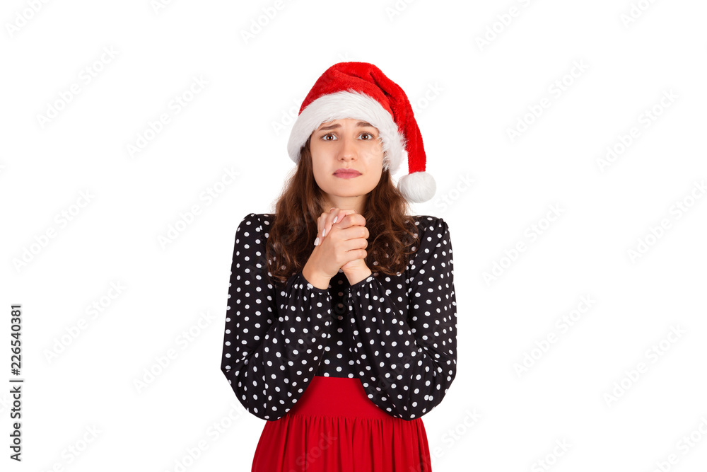 Gloomy cute and timid woman in dress holding hands in pray, asking for apology or help. emotional girl in santa claus christmas hat isolated on white background. holiday concept Gloomy cute and timid woman in dress holding hands in pray, asking for apology or help. emotional girl in santa claus christmas hat isolated on white background. holiday concept