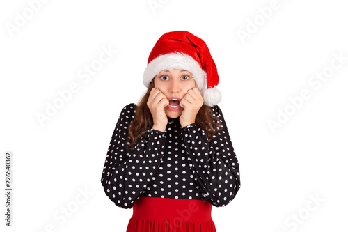 Scared woman looks nervously  biting fingernails and afraid of something. emotional girl in santa claus christmas hat isolated on white background. holiday concept