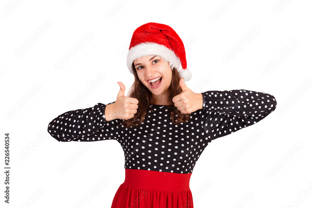 Young woman model in dress showing thumbs up and put hands up looking at camera. emotional girl in santa claus christmas hat isolated on white background. holiday concept Young woman model in dress showing thumbs up and put hands up looking at camera. emotional girl in santa claus christmas hat isolated on white background. holiday concept