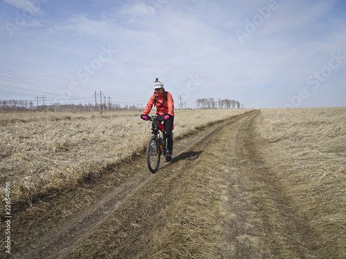 A lone bicyclist in bright outfit rides a field road among the boundless steppe in early spring