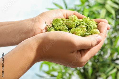 Woman holding fresh green hops on blurred background, closeup. Beer production
