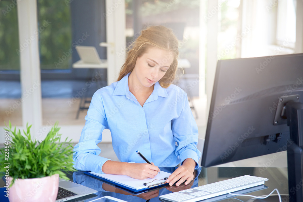 Young sales assistant writing something at office desk Young sales assistant writing something at office desk