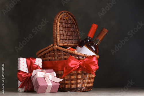 Festive basket with bottles of wine and gifts on table against dark background