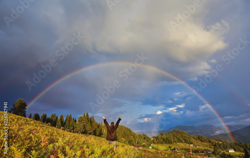 young guy, a tourist, raised his hands and thumbs up, rejoicing at the seen rainbow
