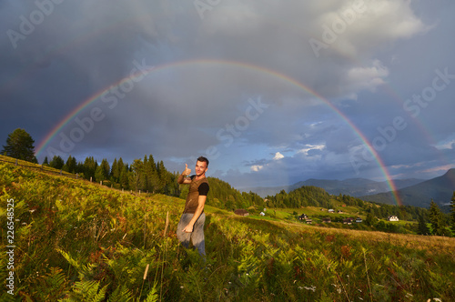 young guy, a tourist, raised his hands and thumbs up, rejoicing at the seen rainbow