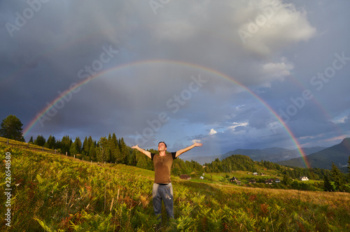 A happy man enjoys the rainbow in the mountains.