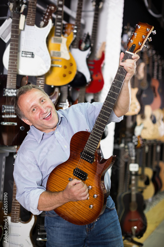 Smiling male is playing on wooden electric guitar
