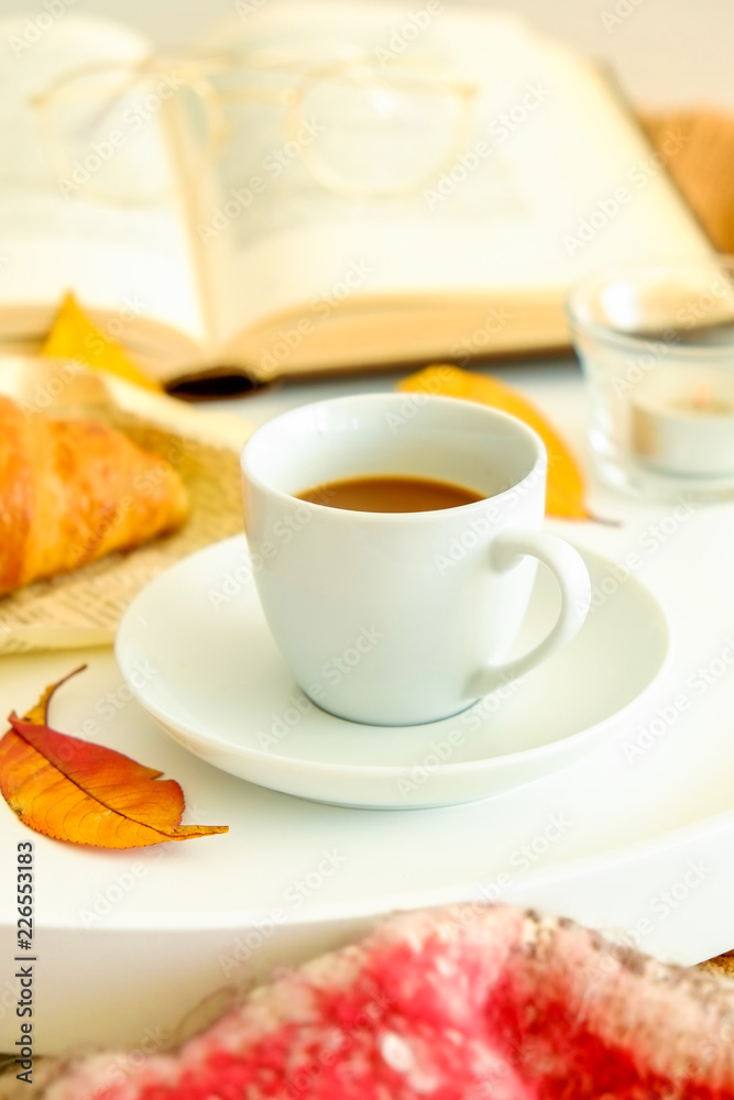 Morning breakfast in bed, white tray with cup of coffee and french croissant, vintage eye glasses and book, yellow autumn leaves, november mood. Close up, top view, background, copy space. Morning breakfast in bed, white tray with cup of coffee and french croissant, vintage eye glasses and book, yellow autumn leaves, november mood. Close up, top view, background, copy space.