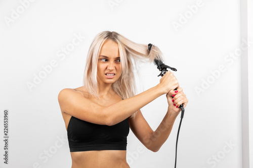 Young girl blonde pulls tangled hair on a white background