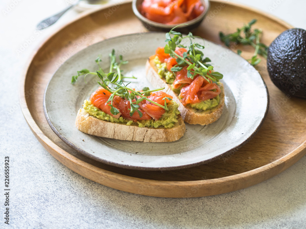 Toasts with avocado and salted salmon with fresh pea sprouts on a plate on a wooden tray Toasts with avocado and salted salmon with fresh pea sprouts on a plate on a wooden tray