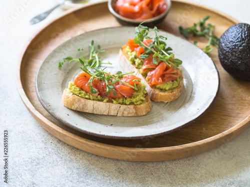 Toasts with avocado and salted salmon with fresh pea sprouts on a plate on a wooden tray