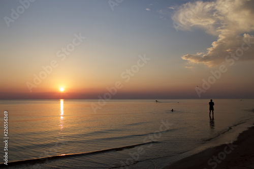 A lonely person standing in the water during the sunset at the beach