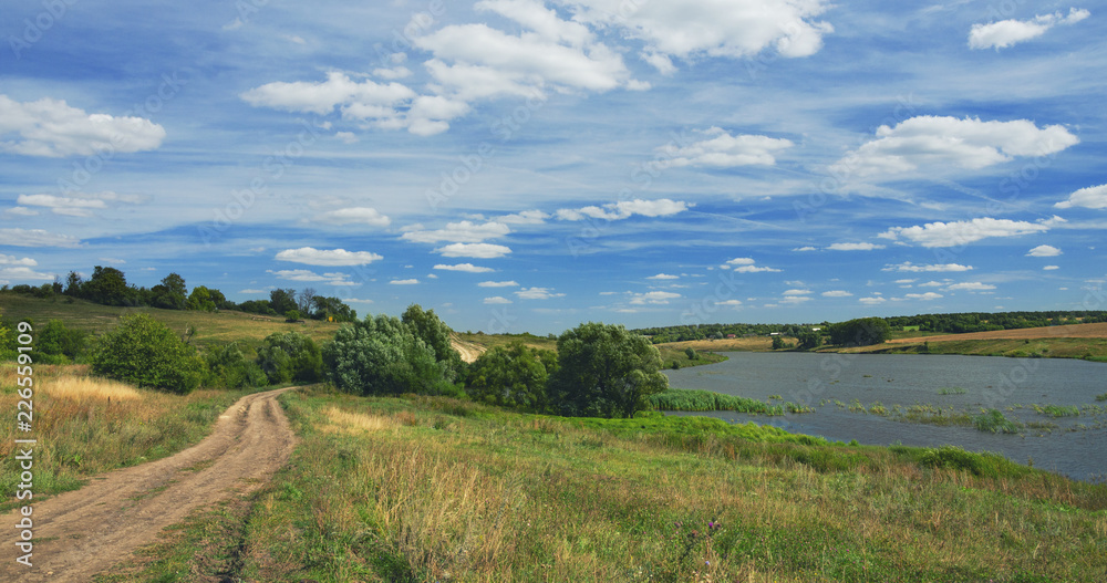 Sunny summer landscape with ground country road,river and beautiful clouds in blue sky.Tula region,Russia.