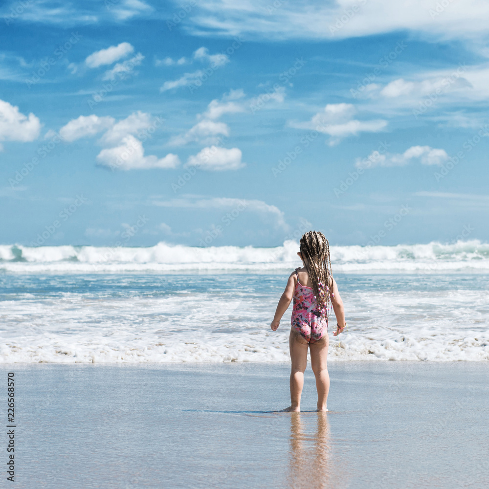 Naklejka premium Little girl standing on the beach and looking at the ocean. Bali. 
