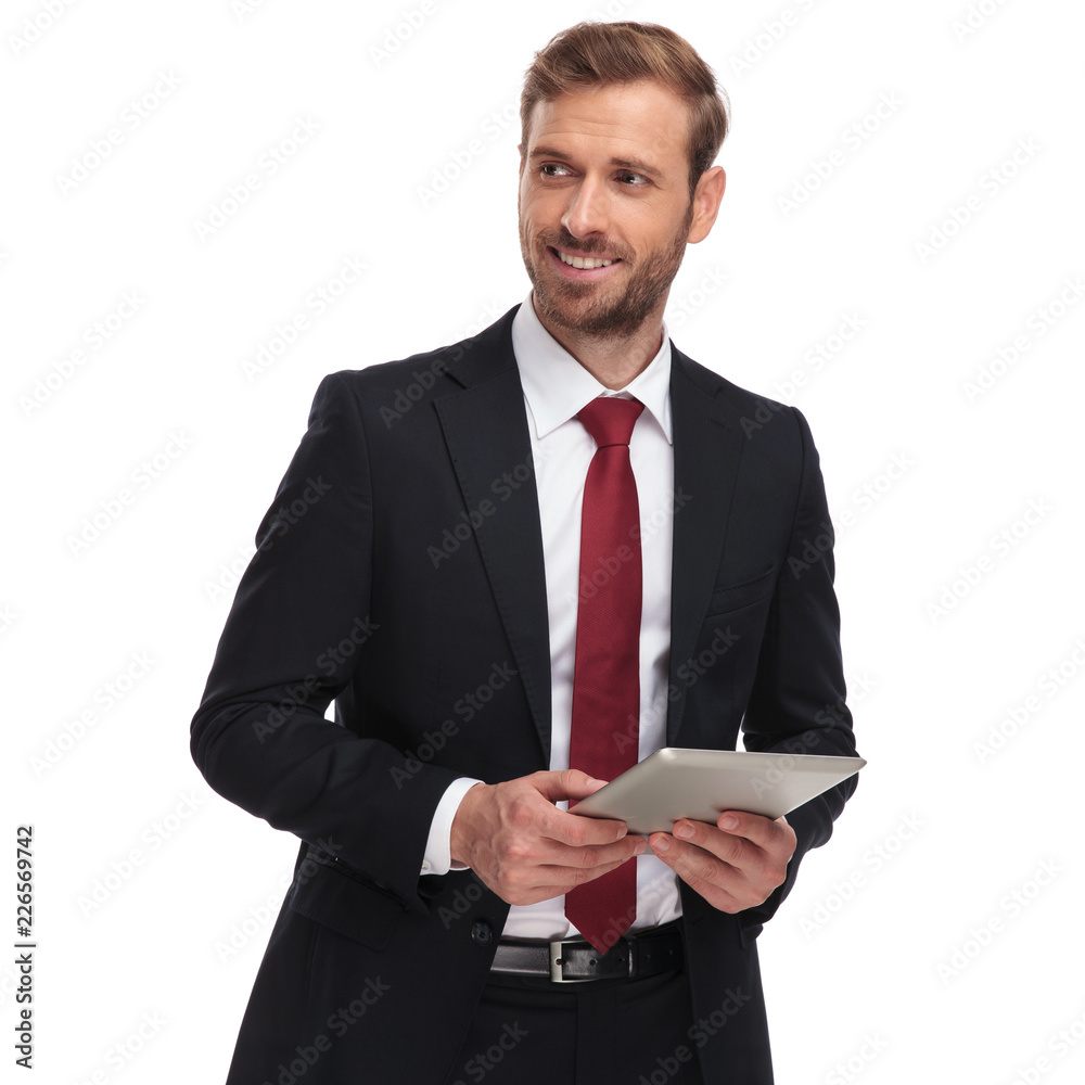 handsome young businessman holding tablet looks to side handsome young businessman holding tablet looks to side