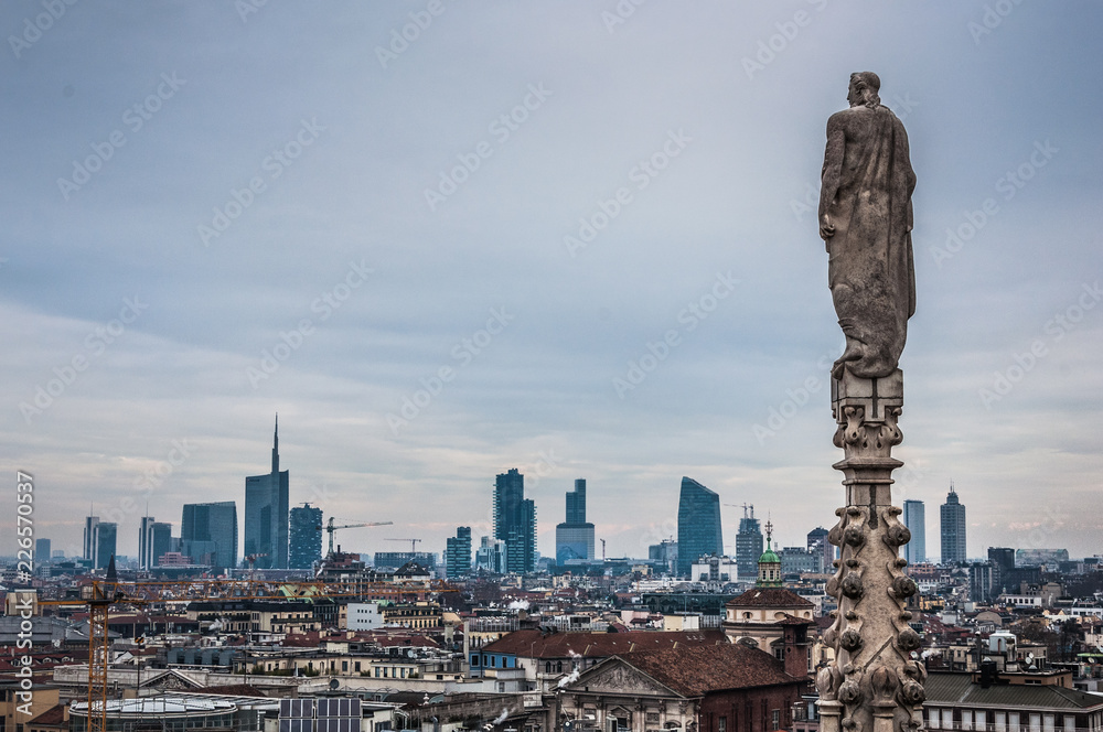 Ancient statue on the roof of Duomo Milano with modern buildings on the background