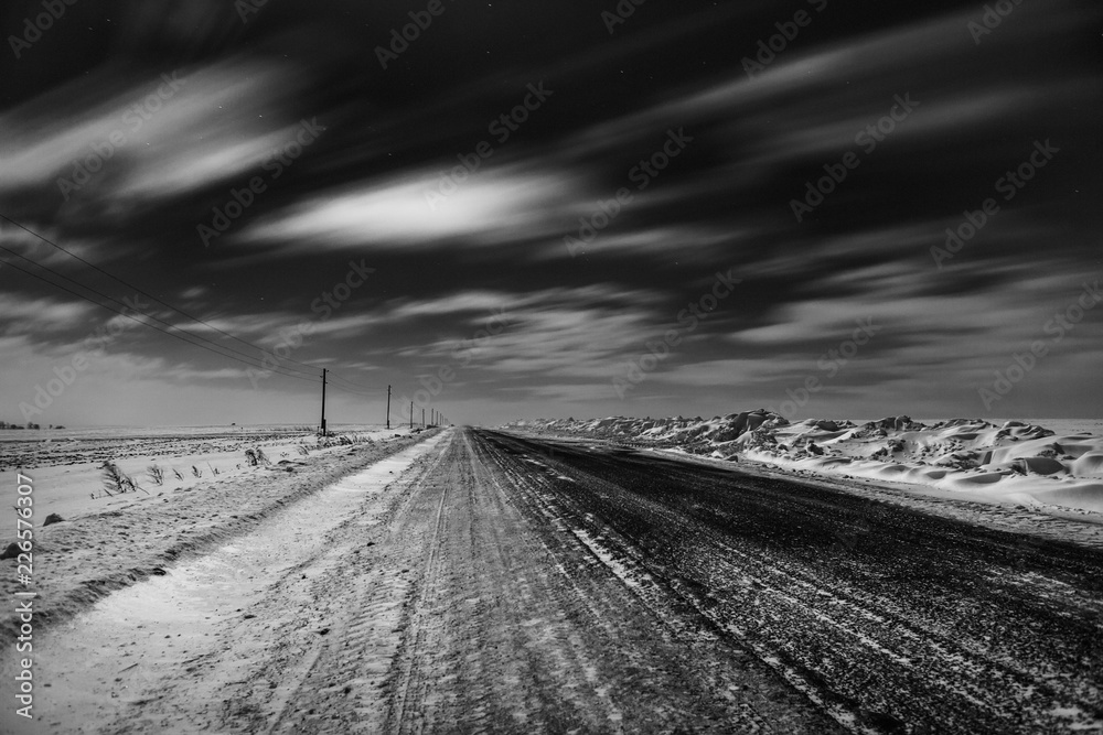 Empty freeway at night. Black and white. Road to the horizon. Clouds, rapidly running across the sky.