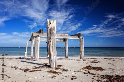 Old ruinous jetty with wooden timber at a sunny morning light at a deserted beach as wide-angle panorama