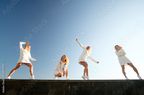 Multiplied collage of young redgead dancing girl, weared in white dress and sneakers, white blue sky background