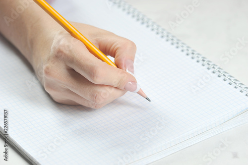 Pencil in the right female hand. Under the hand is a copybook in a cage. Close-up. Light background.