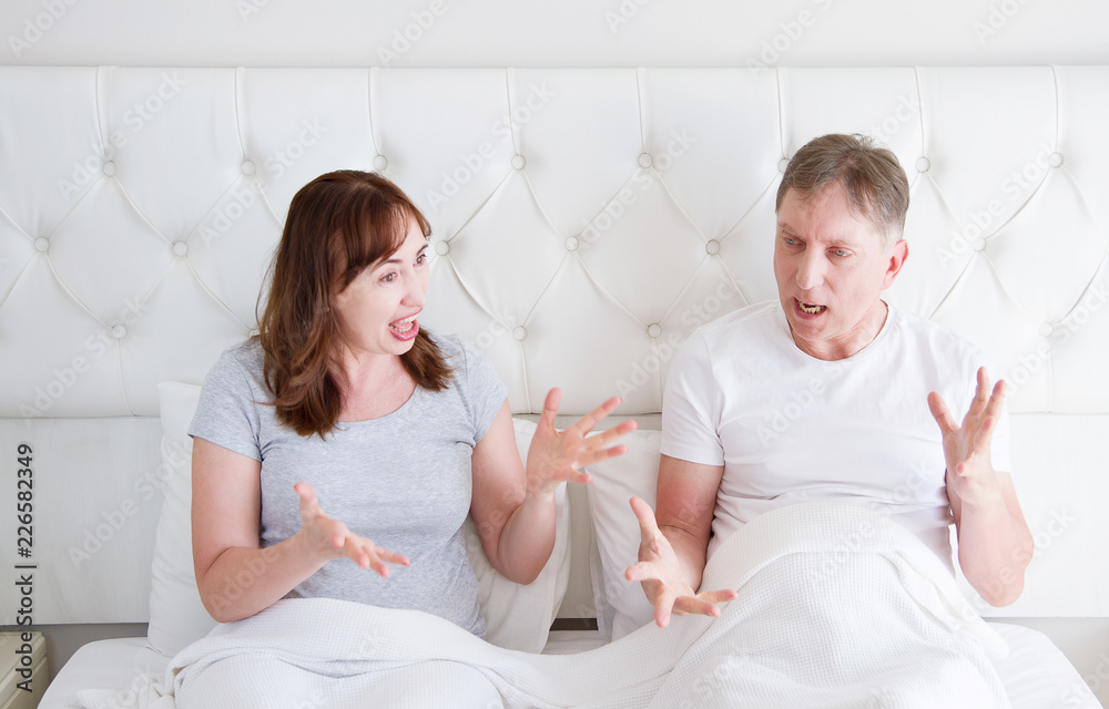 Caucasian middle age family couple angry shouting in bed. Conflict relationship concept. Husband and wife dialogue. Selective focus Caucasian middle age family couple angry shouting in bed. Conflict relationship concept. Husband and wife dialogue. Selective focus