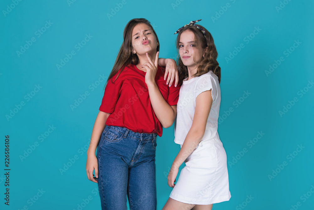 Full height image of two happy cheeky girls , best friends having fun , laughing on blue background. . Wearing stylish casual clothes. Space for text. Cute teenage school girls Full height image of two happy cheeky girls , best friends having fun , laughing on blue background. . Wearing stylish casual clothes. Space for text. Cute teenage school girls