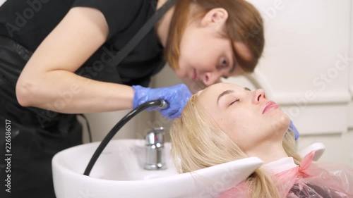A close up of a hairdresser and a blonde holding her head in the backwash basin. The hairdresser has a shower and checks if the water is warm enough and starts washing the hair.