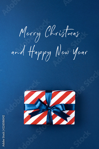Christmas card with gift box wrapped in red striped paper and tied with blue ...