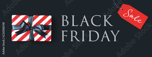 Black friday banner with gift box wrapped in red striped paper and tied with black bow on black background, top view.