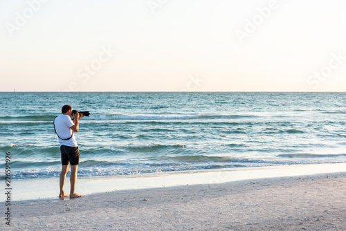 Young man professional photographer hobby taking pictures and video of beach sunset in Florida Siesta Key by Sarasota, beach waves, big camera