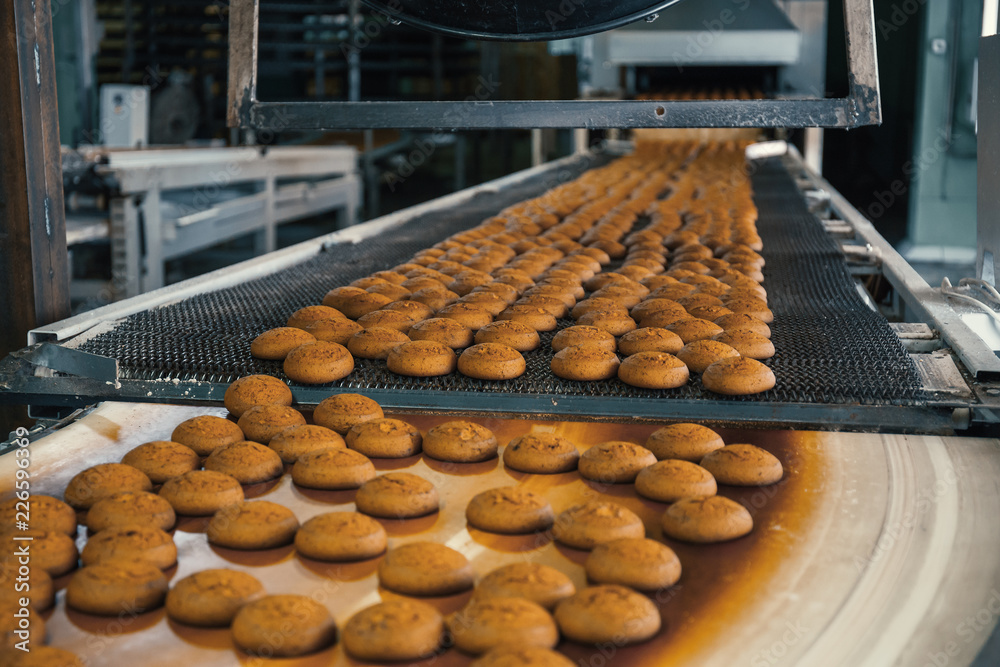 Food factory, production line or conveyor belt with fresh baked cookies. Modern automated confectionery and bakery machinery equipment Food factory, production line or conveyor belt with fresh baked cookies. Modern automated confectionery and bakery machinery equipment