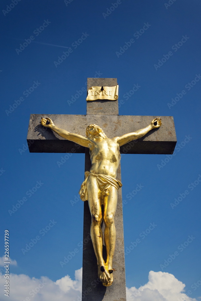 Golden Jesus Christ crucifixion statue, sunny summer day blue sky background, Vrbice, Moravia, Czech Republic Golden Jesus Christ crucifixion statue, sunny summer day blue sky background, Vrbice, Moravia, Czech Republic