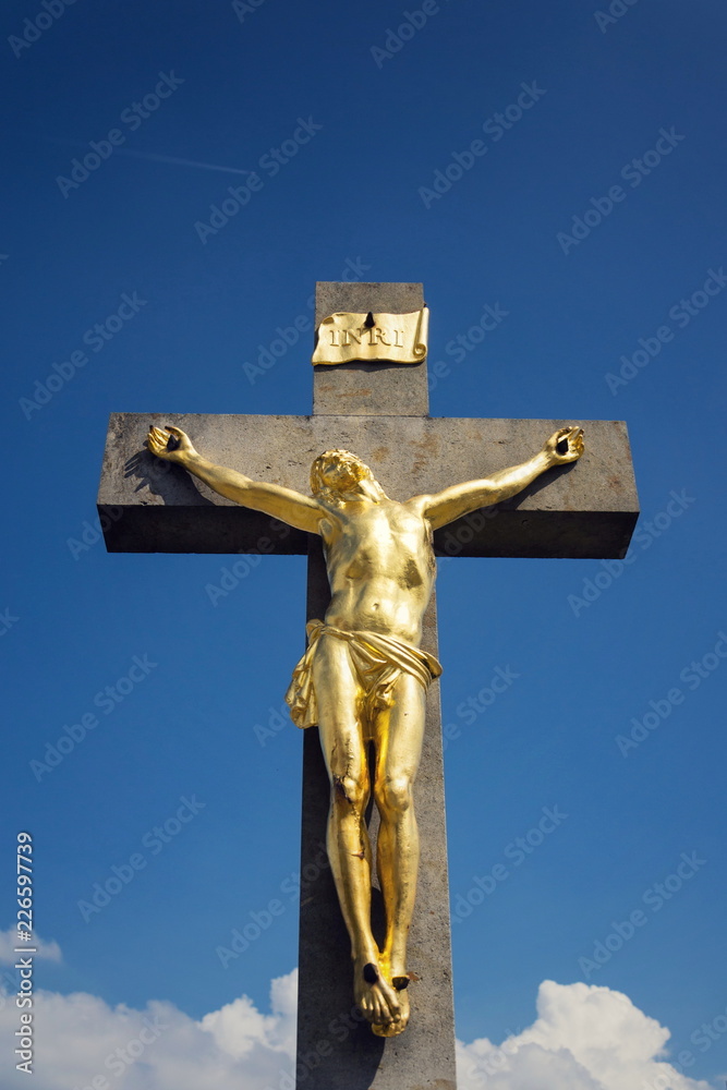 Golden Jesus Christ crucifixion statue, sunny summer day blue sky background, Vrbice, Moravia, Czech Republic