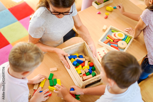 Preschool teacher with children playing with colorful wooden didactic toys at kindergarten