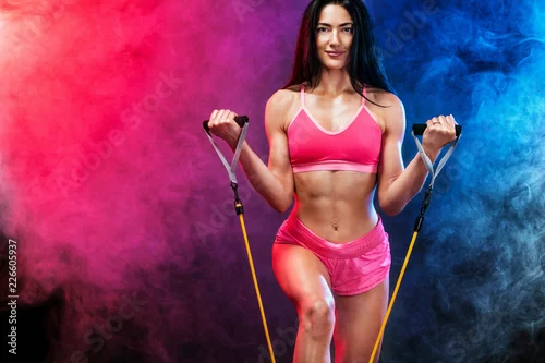 Obraz Mięśni młody sprawny sport kobieta lekkoatletka. Trening z zespołami lub ekspander w siłowni na czarnym tle z dymem colo. Studio strzał.