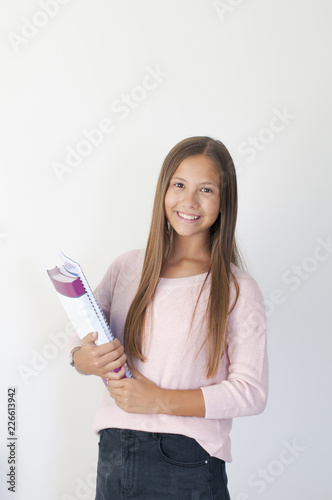 Girl child standing in front of white wall. Girl child holding books in hand.