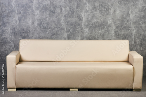 Beige leather sofa against gray textured wall background interior