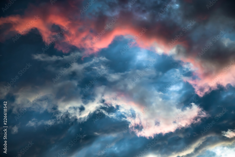 Fototapeta premium Burzliwe niebo z jaskrawoczerwoną poświatą. Kolorowy obraz dramatycznego cloudscape. Niesamowite chmury różowego, białego, szarego koloru na tle wieczornego ciemnego nieba po zachodzie słońca.