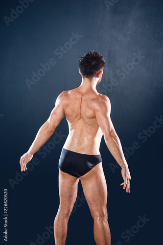 Back of muscular young male athlete posing in black underwear, isolated on dark-blue background
