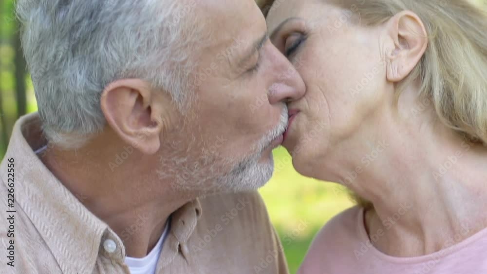 Elderly man taking woman by hand and kissing her in park, happy married couple Elderly man taking woman by hand and kissing her in park, happy married couple