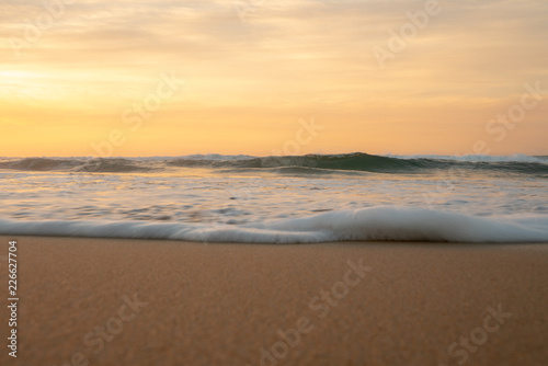Orange sunrise and small foamy waves at the beach