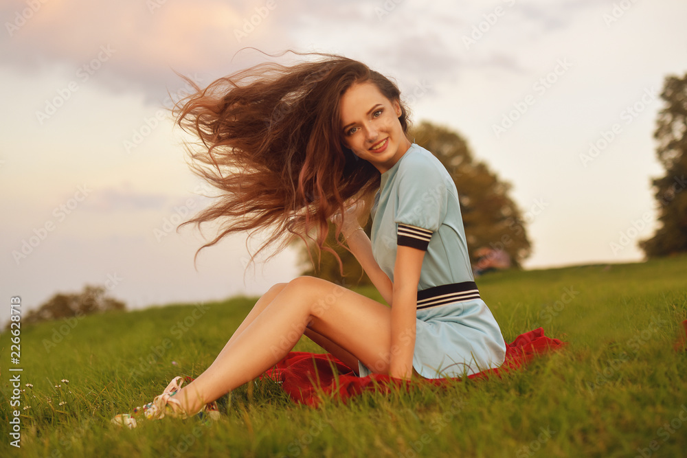 Attractive young woman enjoying her time outside in sunset park. Model girl with magnificent long hair posing outdoor. Beauty, fashion concept. Girl waving her hair in blue dress. Smile pretty girl. Attractive young woman enjoying her time outside in sunset park. Model girl with magnificent long hair posing outdoor. Beauty, fashion concept. Girl waving her hair in blue dress. Smile pretty girl.