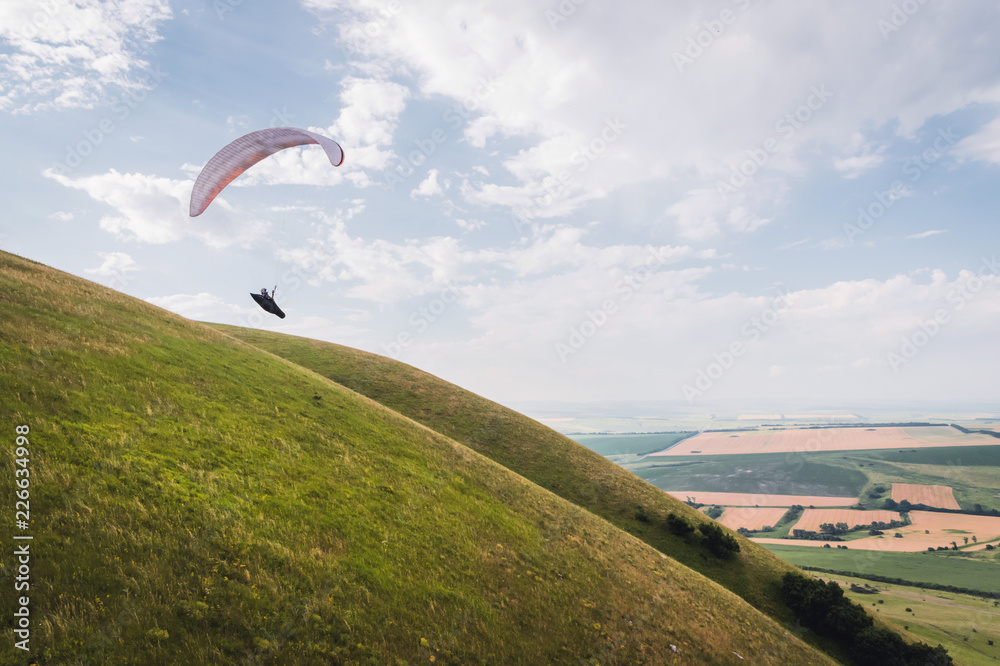 A white-orange paraglider flies over the mountainous terrain A white-orange paraglider flies over the mountainous terrain