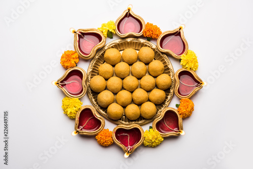 Diwali Rangoli using Diya, flowers and Besan Laddu or Laddoo arrabged over white background, selective focus photo