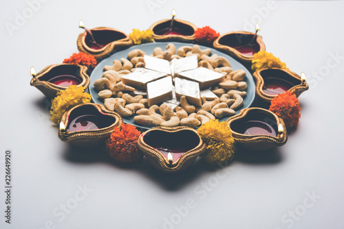 Diwali food Rangoli using Kaju Katli sweet along with Clay diya/lamp and marigold flowers arranged in circular pattern, selective focus
