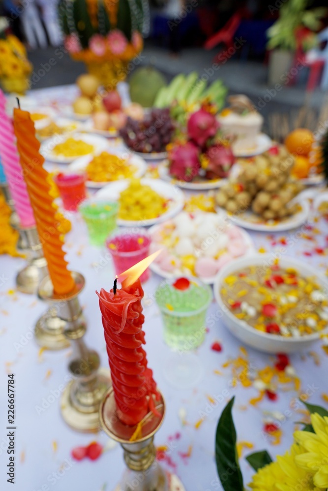 Close up of fire with candle, Holy worship with blurred Thai dessert, colorful water, fruit, flowers and candle to worship on the table, Religion concept, Vertical