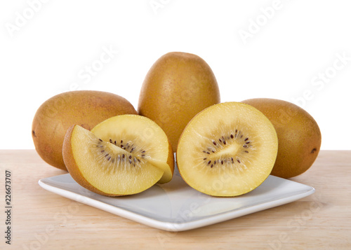 Sungold kiwi sliced in half with whole fruit behind on white plate on wood table. Unlike Green Kiwifruit, new SunGold Kiwifruit have a smooth skin and is less acidic than typical Kiwi fruit.