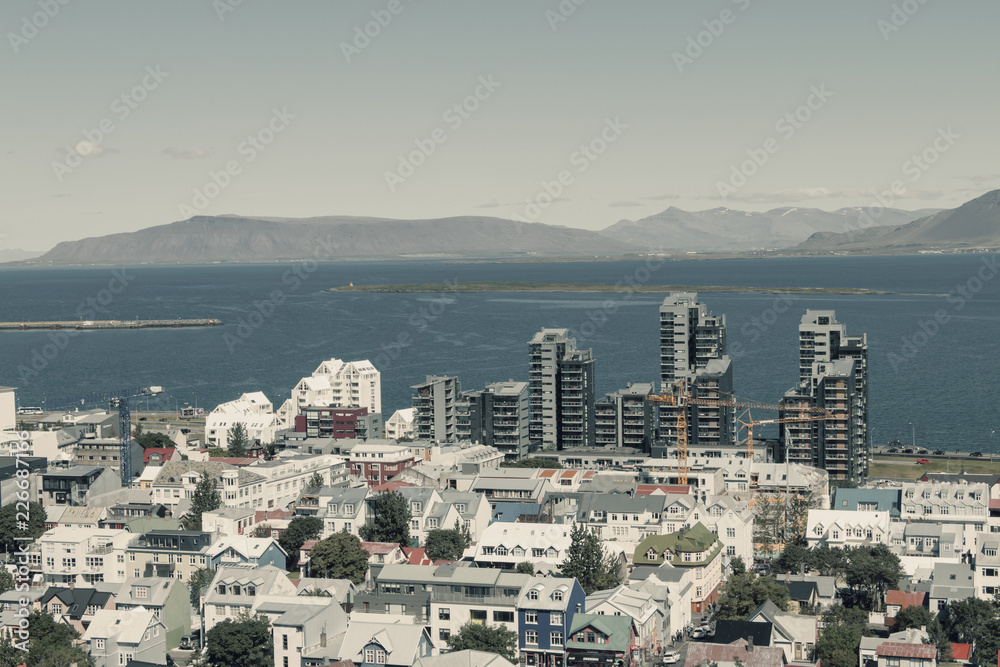 Aerial view on capital of Iceland - city of Reykjavik - ocean bay,  streets, houses, roofing, construction, cranes, mountains, horizon, blue skies, island - on sunny day.